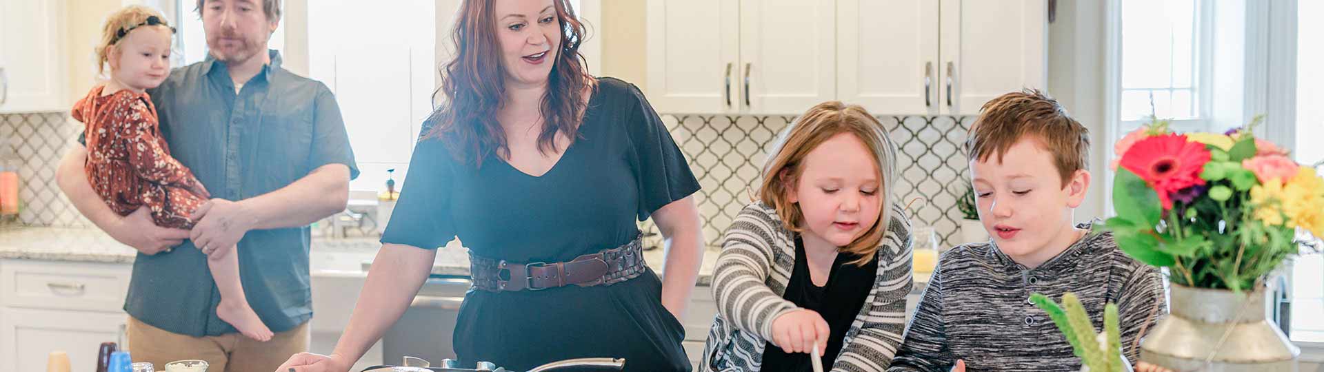 Husband and wife cooking in the kitchen with their three kids